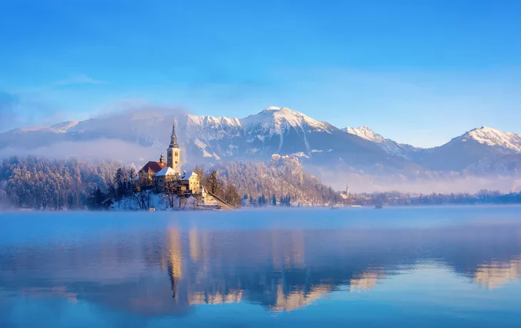 Bleder See an einem sonnigen Wintermorgen mit klarem Himmel und schneebedeckten Bergen