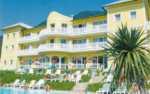 Gelbes Hotelgebäude mit Pool, Sonnenliegen und Palmen im Vordergrund.