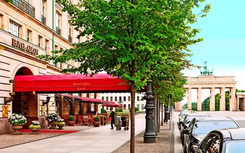 Eingang des Hotel Adlon in Berlin mit rotem Vordach und Bäumen entlang der Straße.