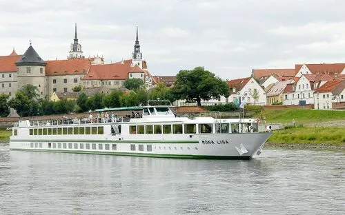 Kreuzfahrtschiff MS Mona Lisa auf einem Fluss vor einer Altstadt mit Kirchtürmen.