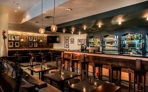Hotelbar mit Theke, hoher Decke und modernem Interieur.