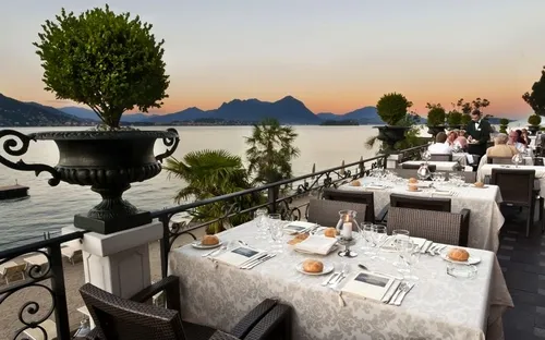 Restaurant-Terrasse mit Seeblick bei Sonnenuntergang, gedeckte Tische, elegante Atmosphäre.