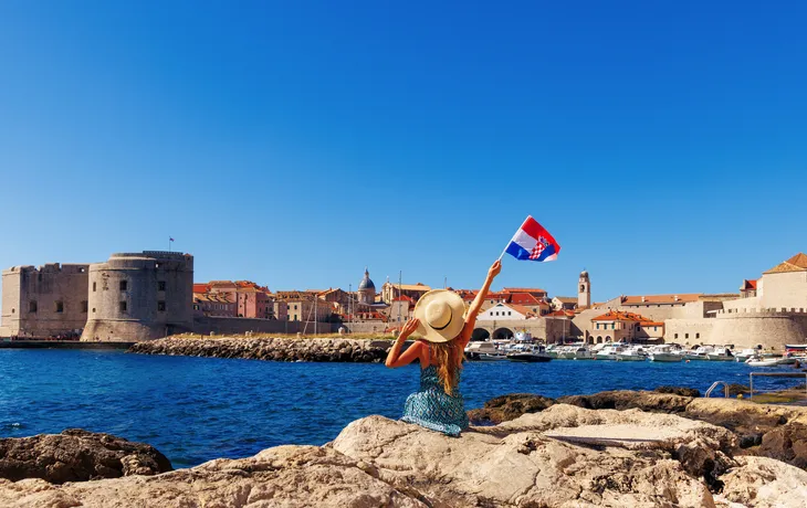  Frau mit kroatischer Flagge, die den Panoramablick auf die Stadtlandschaft von Dubrovnik genießt 