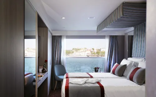 Kabine mit Doppelbett, großem Fenster und Aussicht auf das Wasser.