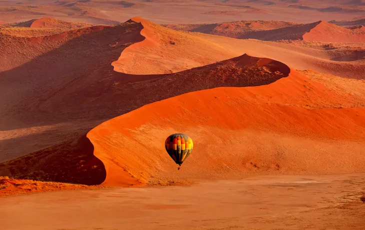 Heißluftballon im Flug gegen orangefarbene Sanddünen im Sossusvlei, Namibia