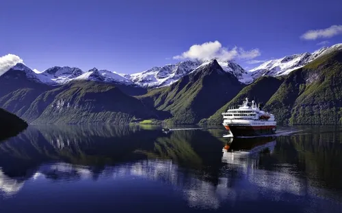 Kreuzfahrtschiff im Hjørundfjord in Norwegen vor schneebedeckten Bergen.
