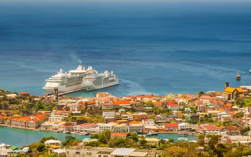 Kreuzfahrtschiff im Hafen vor einer Stadt mit bunten Häusern und blauem Meer im Hintergrund.