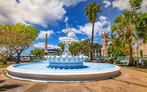 Springbrunnen im Park mit Palmen und Kirche im Hintergrund bei sonnigem Himmel.