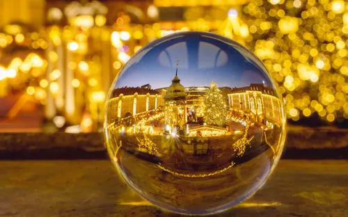 Kugel reflektiert beleuchteten Weihnachtsmarkt mit Baum und Lichtern.