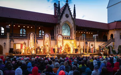 Außenbühne mit mittelalterlich gekleideten Schauspielern und Publikum.