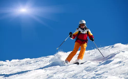 Person fährt auf Skiern einen sonnigen Hang hinunter.