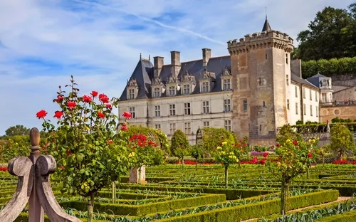 Ein Schloss mit gepflegten Gärten und blühenden Rosen im Vordergrund.