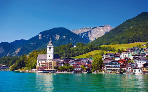 Seeuferstadt mit Kirche und Bergen im Hintergrund bei klarem Wetter.