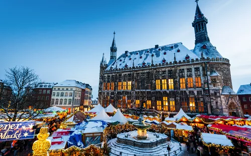 Aachener Weihnachtsmarkt mit festlich geschmückten Marktständen vor dem historischen Rathaus. Die Szene zeigt winterliche Beleuchtung und weihnachtlichen Trubel.