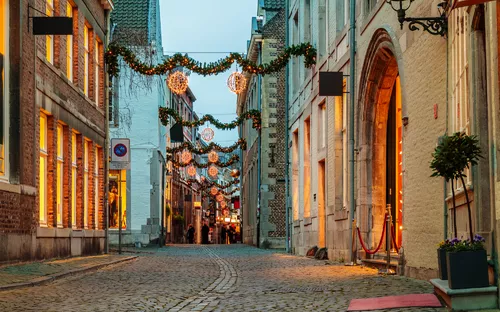 Einkaufsstraße in Maastricht, geschmückt mit Weihnachtsbeleuchtung, die Bäume und Gebäudefassaden erhellt.