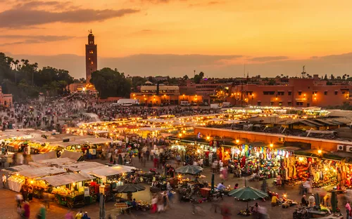 Marktplatz in Marrakesch bei Sonnenuntergang mit vielen Menschen und Ständen.