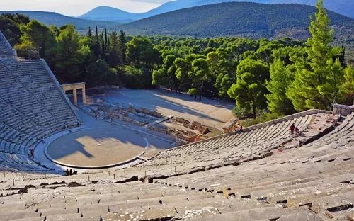 Antikes Amphitheater mit Wald und Bergen im Hintergrund.