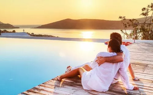 Ein Paar sitzt am Rand eines Pools und blickt auf das Meer bei Sonnenuntergang.