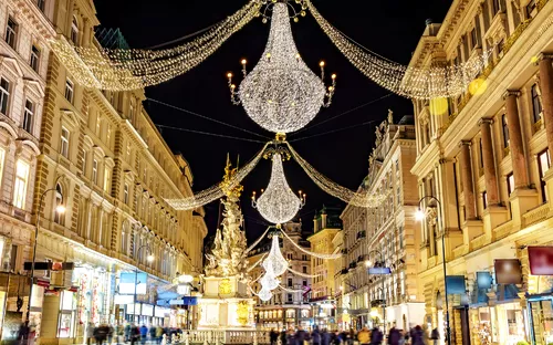 Beleuchtete Einkaufsstraße mit großen Kronleuchtern bei Nacht.