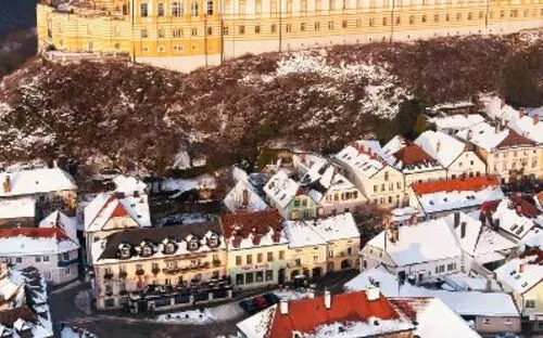 Blick auf ein barockes Kloster auf einem Hügel in einer verschneiten Stadt mit roten Dächern.