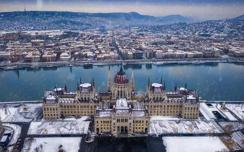 Luftaufnahme des verschneiten Parlamentsgebäudes in Budapest am Flussufer.