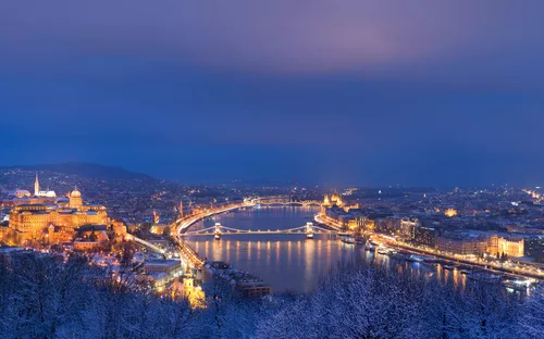 Winterliche Stadtansicht mit Fluss und beleuchteten Gebäuden bei Dämmerung.