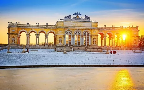 Barockes Bauwerk im Schnee bei Sonnenuntergang, mit Menschen im Vordergrund.