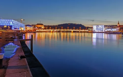 Stadtansicht bei Nacht mit beleuchteten Gebäuden und Wasserreflexionen.
