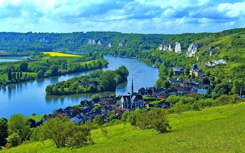 Landschaft mit Fluss, Hügeln und Dorf im Vordergrund.