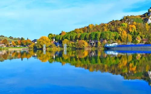 Flusslandschaft mit Burgruine, herbstlichen Bäumen und Spiegelung im Wasser.