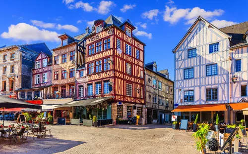 Historische Fachwerkhäuser an einem sonnigen Platz mit Cafés und blauem Himmel.