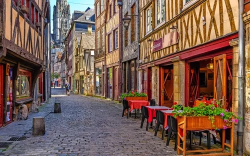 Gepflasterte Altstadtstraße mit Fachwerkhäusern und Straßencafé, Radfahrer im Hintergrund.