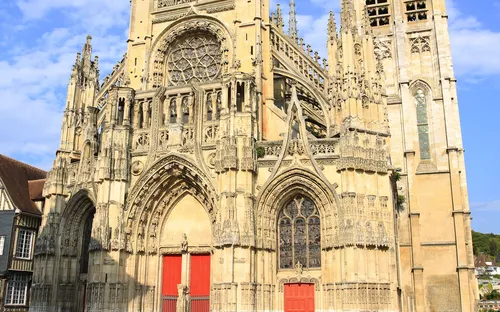 Historische gotische Kathedrale mit hohen Türmen und roten Türen bei blauem Himmel.