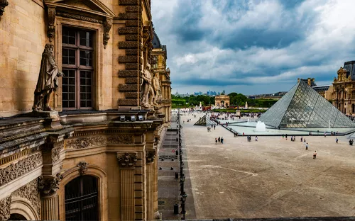 Blick auf den Louvre mit der Glaspyramide und umliegenden Gebäuden bei bewölktem Himmel