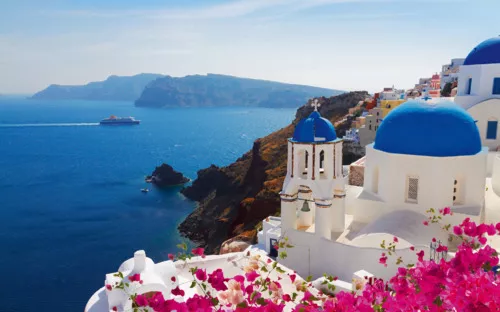 Blau-weiße Gebäude mit blauen Kuppeln und blühendem Bougainvillea-Meerblick