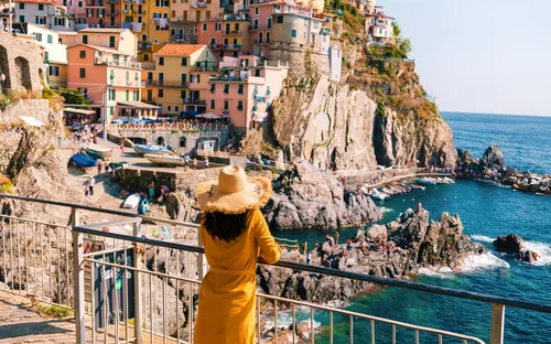 Frau betrachtet bunte Küstenhäuser und Meer in Cinque Terre, Italien.
