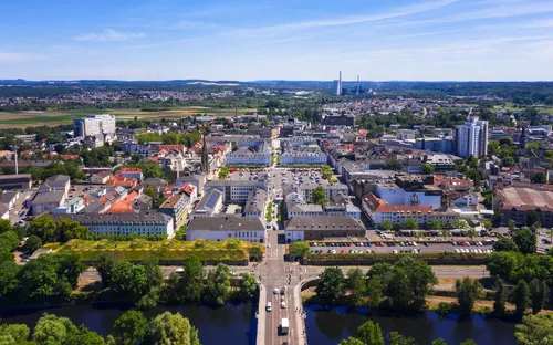 Stadtansicht mit Fluss und Brücke im Vordergrund bei klarem Himmel.