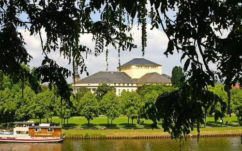 Boot auf einem Fluss vor einem großen Gebäude, umgeben von Bäumen.