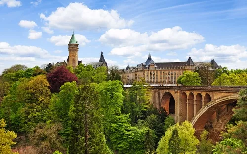 Schloss und Viadukt in grüner Landschaft unter blauem Himmel.