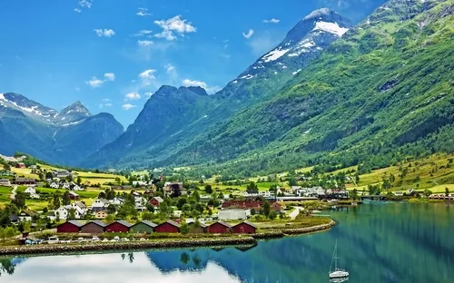 Norwegisches Fjorddorf mit Bergen und Häusern am Ufer, segelndes Boot im Wasser.