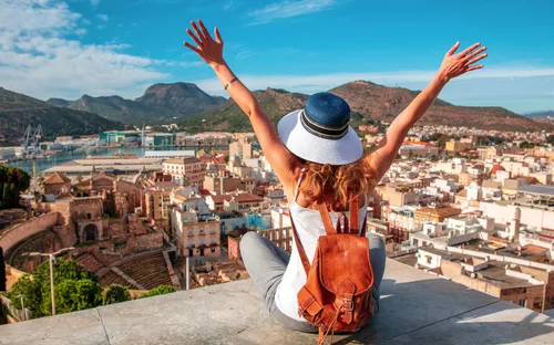 Frau mit Hut und Rucksack blickt auf Stadt und Berge bei sonnigem Wetter