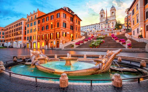 Spanische Treppe in Rom bei Sonnenuntergang mit Barcaccia-Brunnen im Vordergrund.
