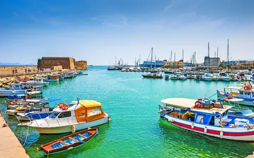 Boote im Hafen mit klarem türkisem Wasser und einem alten Festungsgebäude im Hintergrund.