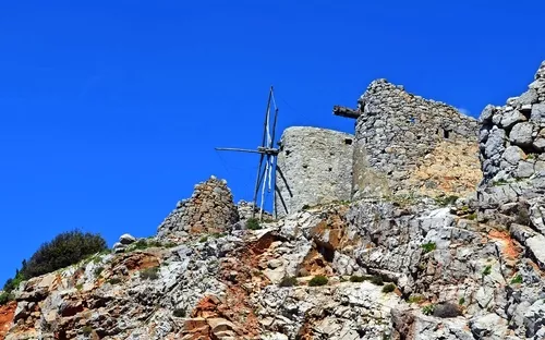 Alte Windmühlen aus Stein auf einem felsigen Hügel unter einem klaren blauen Himmel.