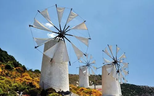 Drei traditionelle Windmühlen auf einem Hügel bei klarem Himmel.