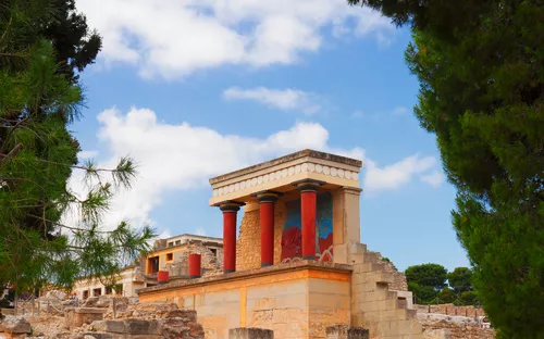 Ruinen des Palastes von Knossos in Kreta mit blauen Himmel und Bäumen im Vordergrund.