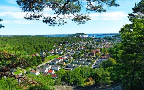 Luftaufnahme einer kleinen Stadt, umgeben von viel Grün und Wald, im Hintergrund das Meer.
