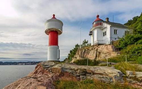 Leuchtturm und weißes Haus auf Klippe vor bewölktem Himmel am Meer.