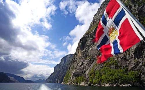 Norwegische Fahne weht über Fjordlandschaft mit Bergen und Fluss.