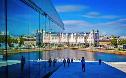 Personen vor moderner Glasfassade mit Blick auf Wasser und historische Gebäude im Hintergrund.